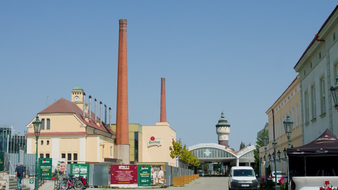 Large brewery buildings, chimneys, and clocktower with vehicles and pedestrians in outdoor scene