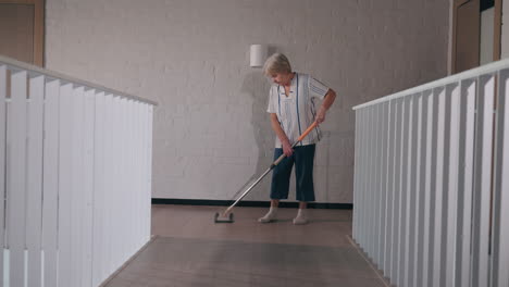 elderly woman mopping a hallway