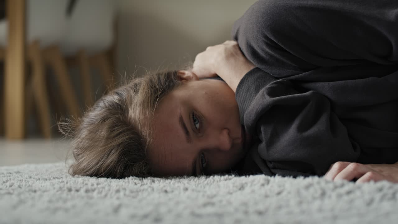 Donna caucasica sdraiata sul tappeto in casa con problemi di salute mentale.