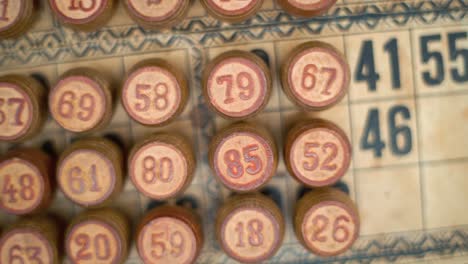primer plano cinematográfico plano liso a la izquierda, disparado desde arriba de un bingo barriles de madera, figuras de madera, viejos números de fondo, juego de mesa vintage, número de suerte, iluminación profesional, cámara lenta 120 fps