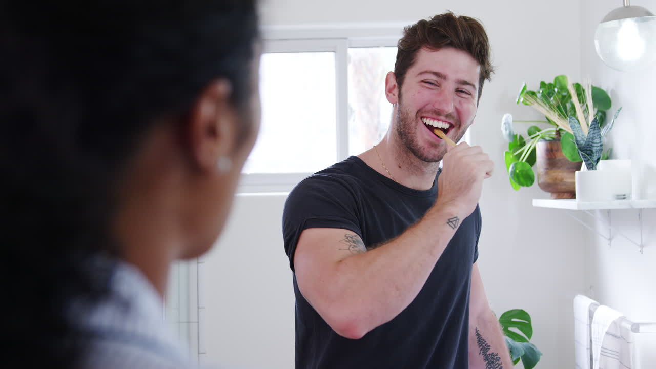 파자마를 입은 부부는 아침에 싱크대 화장실에 서서 치아를 고 있습니다.