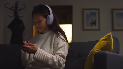 woman relaxing on the couch, listening to music on her phone