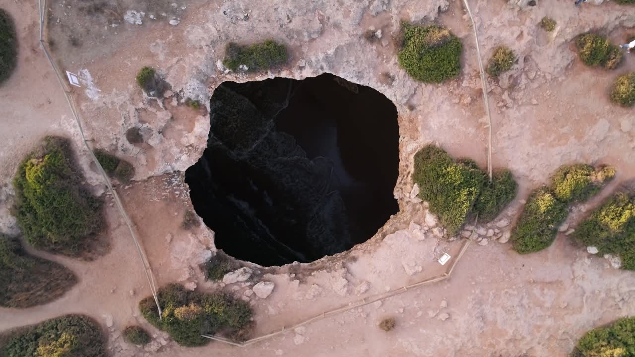 Top down spiralling drone shot rising above Benagil cave ceiling opening. The tide and waves wash up the beach inside.