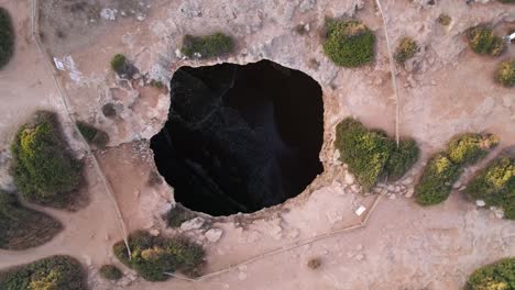 top down spiralling drone shot rising above benagil cave ceiling opening. the tide and waves wash up the beach inside.