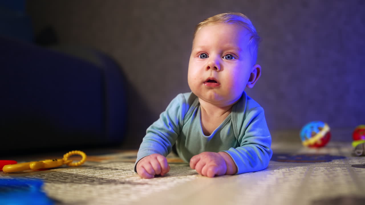 Lovely big-eyed baby looking ahead with surprise. Beautiful infant lies on the floor close up.
