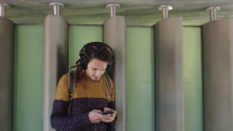 retrato de un joven de raza mixta con auriculares escuchando música y enviando mensajes de texto por teléfono
