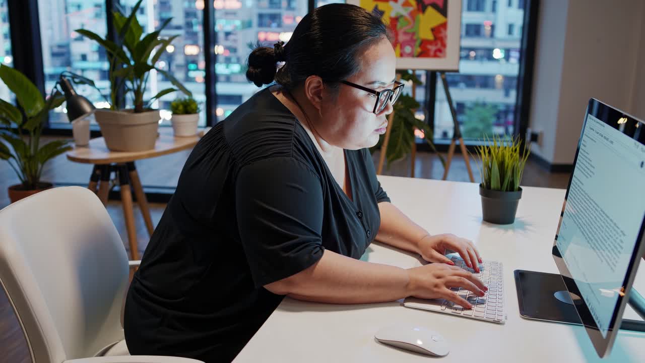 A woman types on a computer in a modern office, captured from a side angle