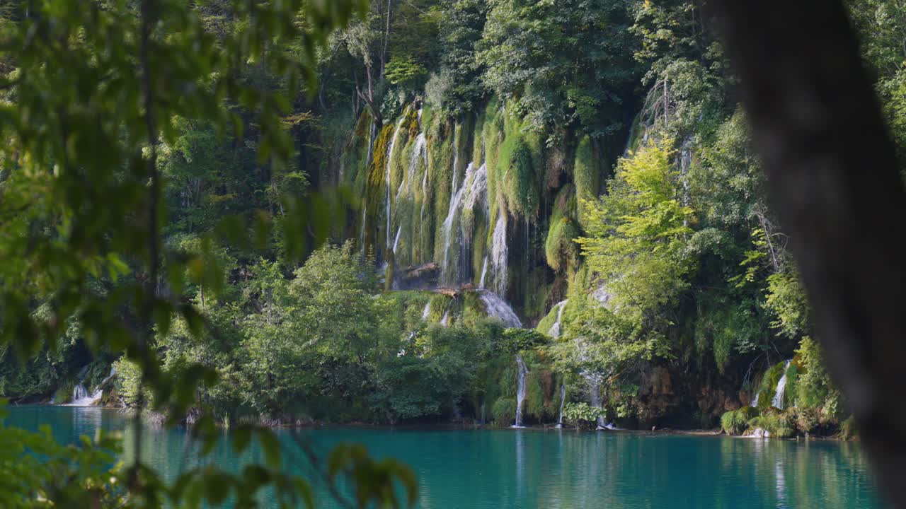 Cascate e lago turchese incorniciati dai rami della foresta nel Parco Nazionale dei Laghi di Plitvice, Croazia
