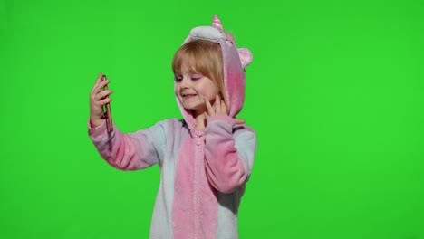 Child-girl-in-unicorn-costume-pajamas-using-smartphone,-kid-emotionally-makes-selfie-on-mobile-phone