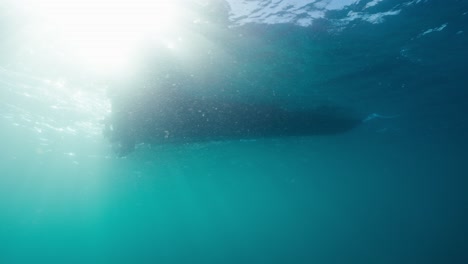 underwater clip showing the hull of a boat as it floats on the ocean surface with the suns rays shining through the water