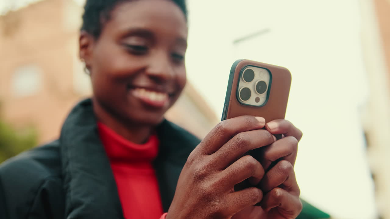 Giovane donna afroamericana felice che usa lo smartphone all'aperto.