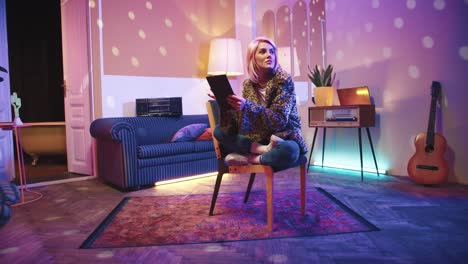 Young-stylish-caucasian-woman-sitting-on-a-chair-and-using-tablet-in-a-retro-party-at-home