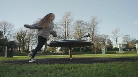 A-young-girl-playing-in-the-local-park-on-the-merry-go-round-surrounded-by-trees