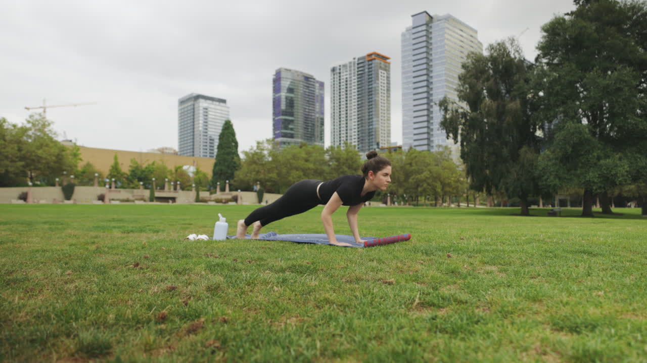 tiro hacia adelante de una mujer caucásica haciendo yoga chaturanga dandasana en un parque con el horizonte de seattle en segundo plano
