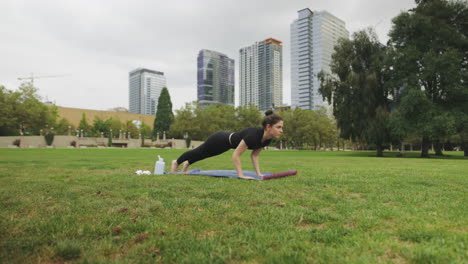 Tiro-Hacia-Adelante-De-Una-Mujer-Caucásica-Haciendo-Yoga-Chaturanga-Dandasana-En-Un-Parque-Con-El-Horizonte-De-Seattle-En-Segundo-Plano