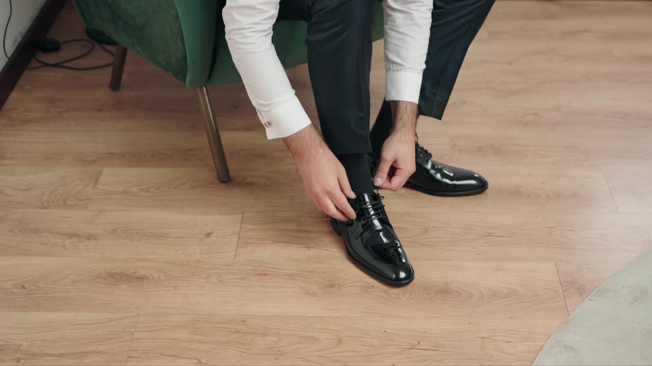 Man in black suit and white shirt ties black polished shoes on wooden floor