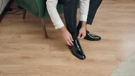 man in black suit and white shirt ties black polished shoes on wooden floor