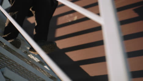 vista de la pierna de una persona vestida de negro que desciende por la escalera sosteniendo un maletín, con la luz del sol proyectando sombras dramáticas en la pared en un entorno urbano moderno