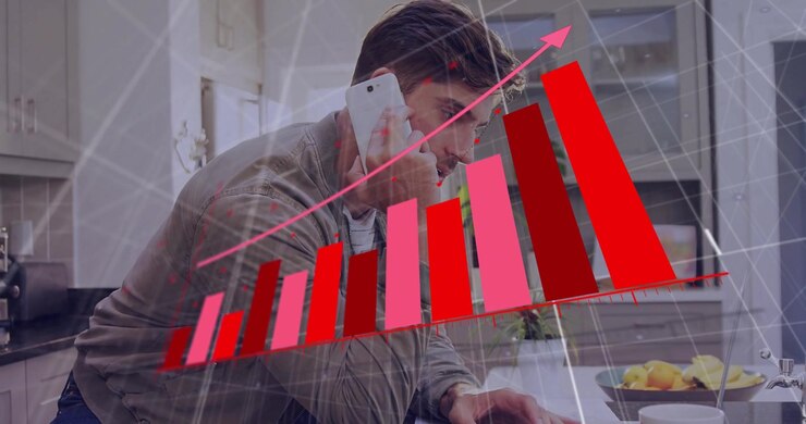 Man leaning on kitchen counter using smartphone, analyzing financial bar chart with arrow on laptop