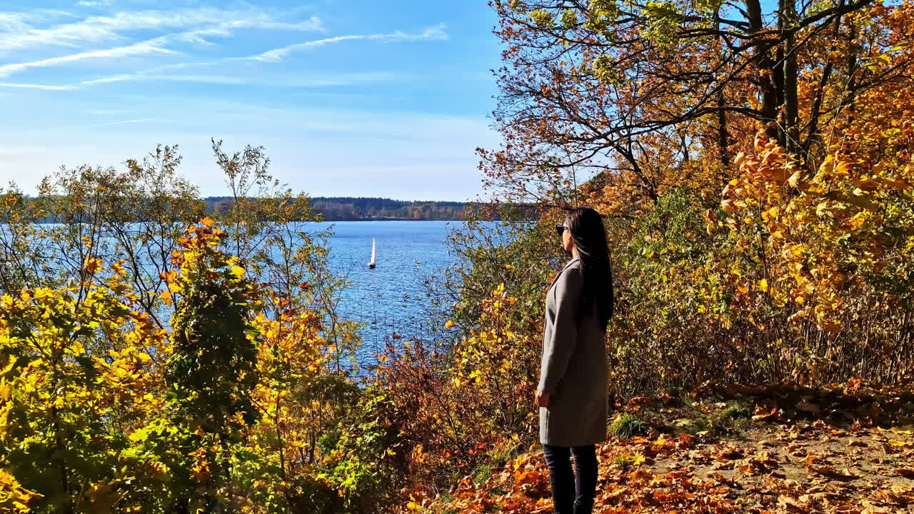 Autumn view of woman by a lake with sailboat in Lielvarde, Latvia