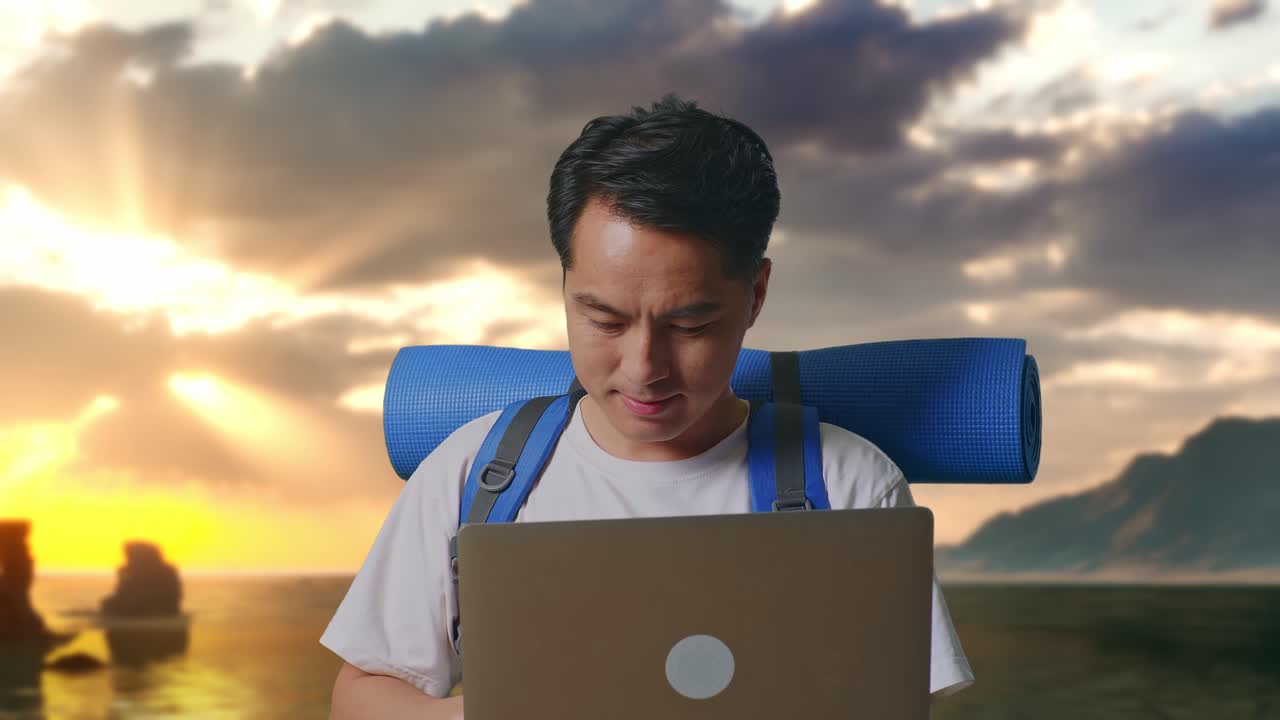 Close-up van een Aziatische mannelijke wandelaar met een bergsportrugzak die een laptop gebruikt op het strand