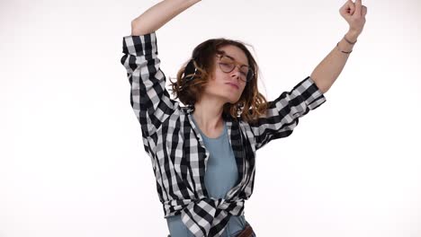 Mujer-Joven-Con-Camisa-A-Cuadros-Escuchando-Música-Con-Auriculares,-De-Pie-Sobre-Un-Fondo-Blanco-Aislado,-Muy-Feliz-Y-Emocionada-Bailando-Con-Los-Brazos-Levantados,-Se-Mueve-Emocionalmente.-Camara-Lenta