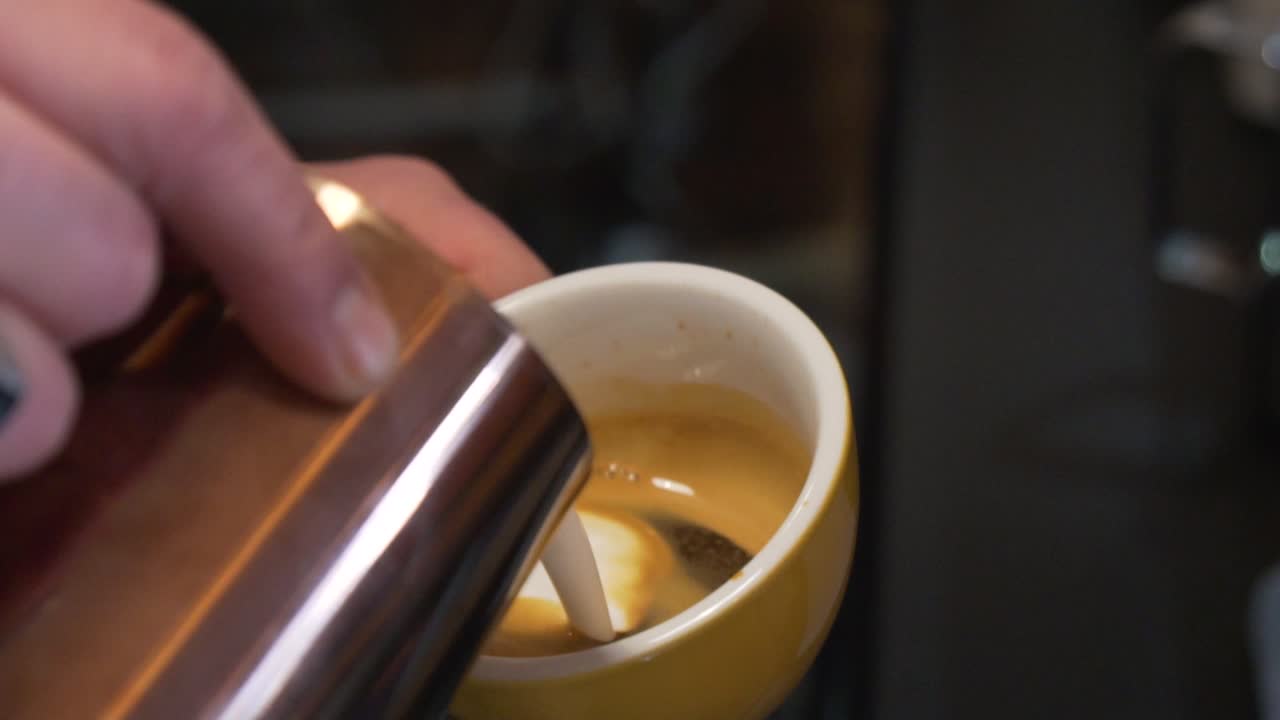 manos de barista vertiendo leche en una taza de café
