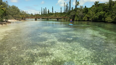 Isle-of-Pines-New-Caledonia-woman-using-a-paddleboard-in-a-paradise-cove---low-altitude-aerial-flyover