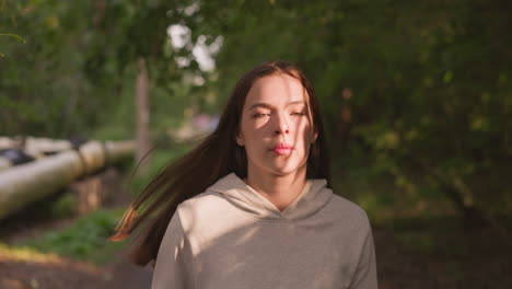 red-haired woman runner prepares for competition in city park. concentrated lady trains to increase endurance before marathon running in nature. sunlight falls on lady face