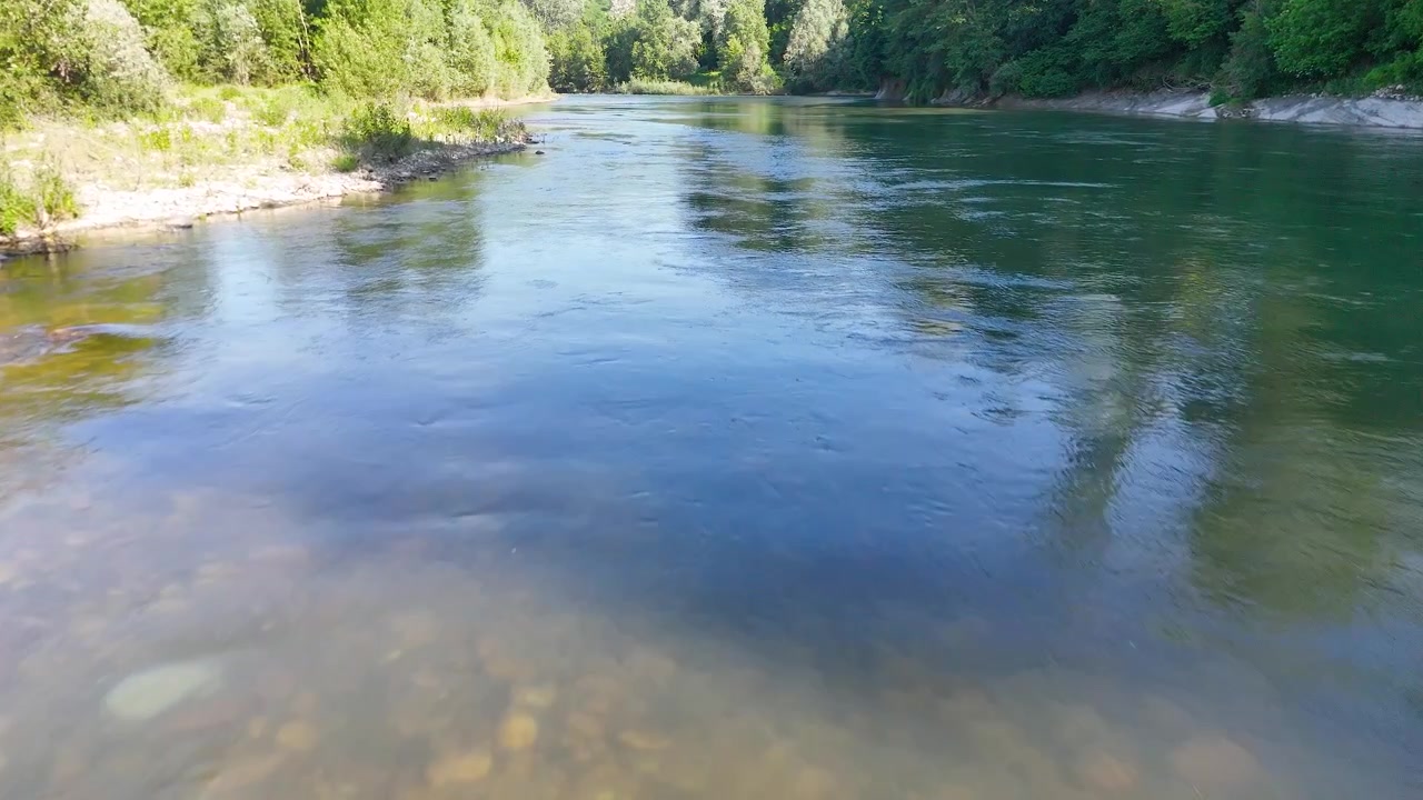 Inquadratura ampia di un fiume limpido che scorre sulle rocce con sponde di foresta verde lussureggiante