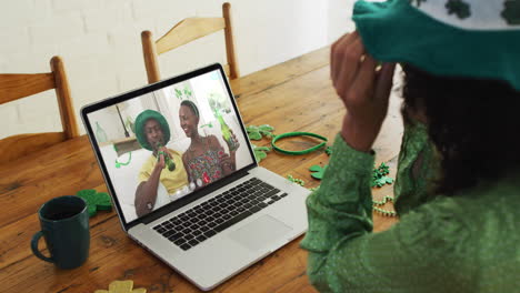 mujer caucásica en llamada de video portátil celebrando el día de san patricio con amigos