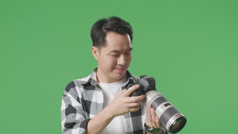 close up of asian photographer looking at the pictures in the camera and smiling being satisfied with the result while standing on green screen background in the studio