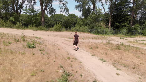 drone-shot-of-a-man-walking-trough-a-dry-barren-land-with-trees-in-the-background-on-a-sandy-path