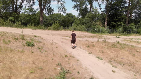 disparo de un dron de un hombre caminando a través de una tierra seca y estéril con árboles en el fondo en un camino de arena