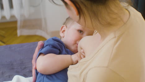 Schulteraufnahme-Einer-Jungen-Frau,-Die-Ihren-Kleinen-Jungen-Stillt,-Während-Sie-Zu-Hause-Auf-Dem-Bett-Sitzt-1