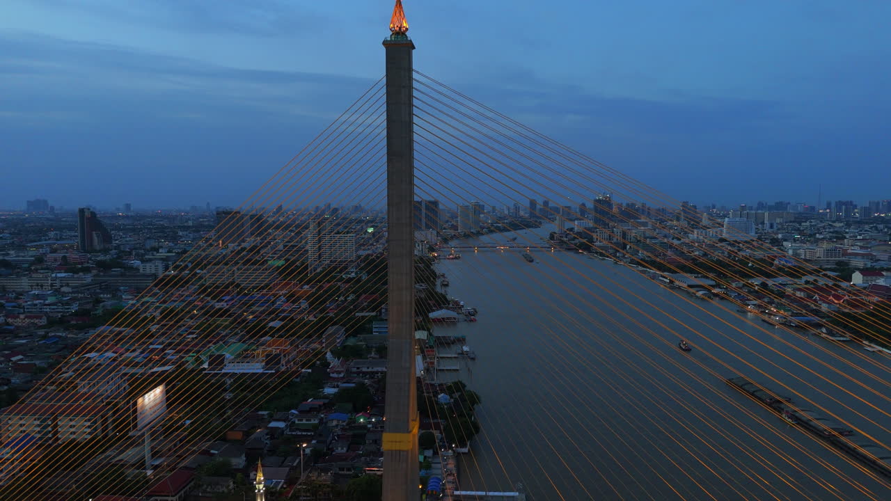 Dusk drone rotation around Rama VIII Bridge in Bangkok, showing illuminated cables, river traffic, a glowing moon, and the distant skyline across the Chao Phraya River