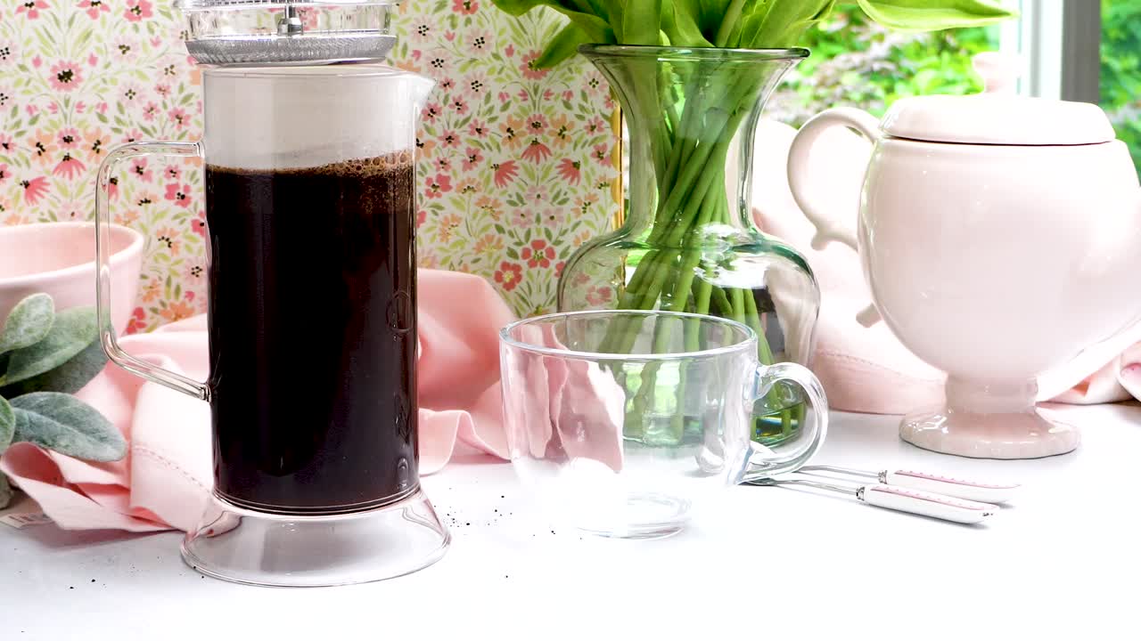 French Press made of clear glass being used to make a hot coffee. Pastel colors in a scene making hot coffee. Fresh ground coffee for brewing using a French Press method of extraction.