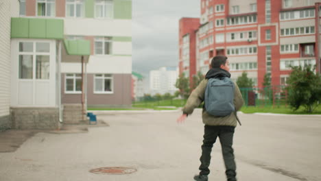back view of kid with backpack running toward school building on cloudy day showing determination and energy in motion across paved courtyard with green and beige walls in educational environment