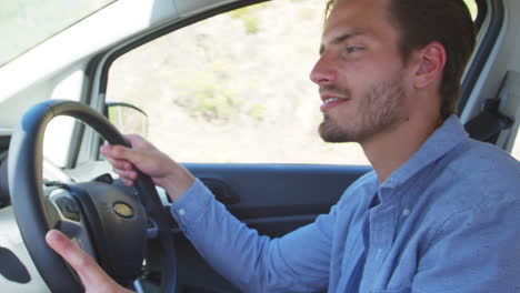 Un-Joven-Sonriente-Conduciendo-Un-Coche-En-Un-Viaje-Por-Carretera