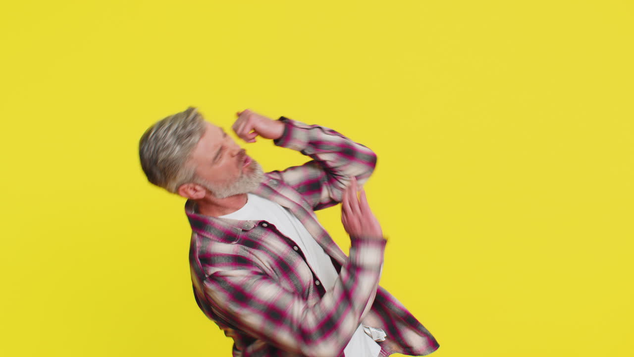 Mature man strums playing on invisible imaginary guitar energetically dancing rocknroll music