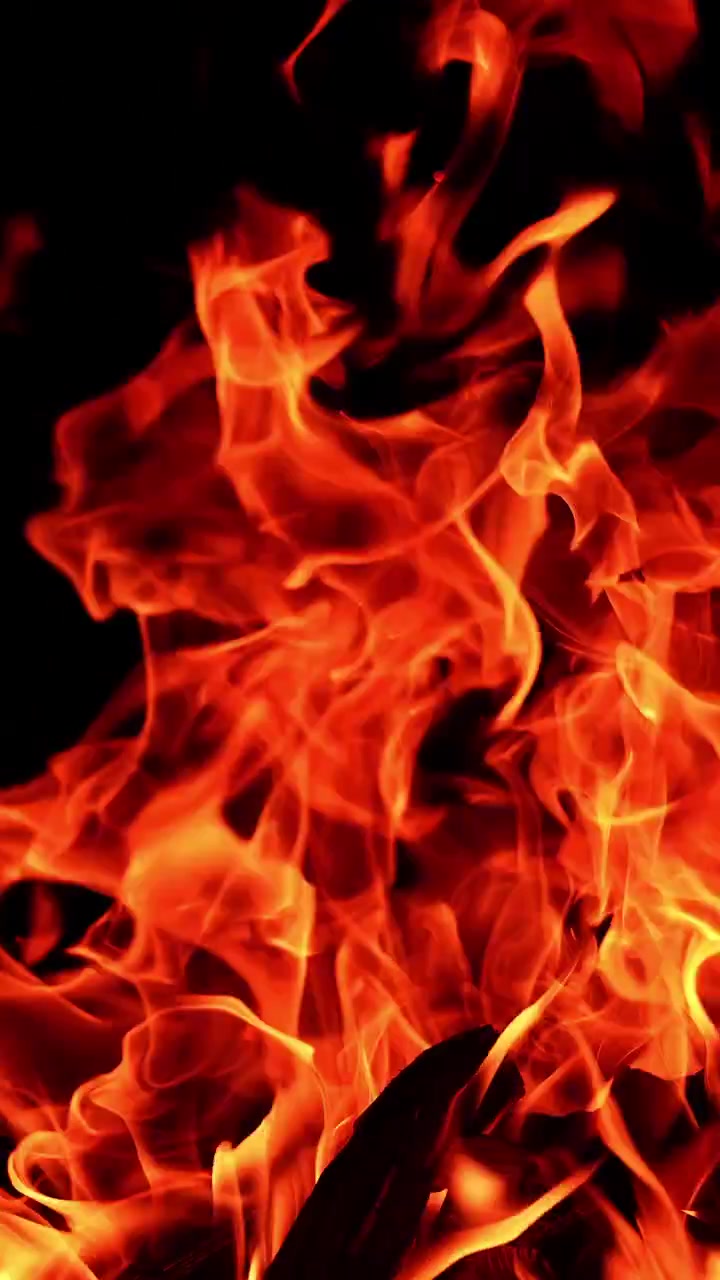 Grande falò che si innalza nella notte buia. Fiamme pericolose si piegano di lato al vento. Video verticale.