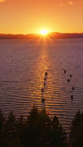 yachts and boats holding still on the waters of amazing lake in the rays of setting sun. mountainous horizon and orange sky at backdrop. vertical video