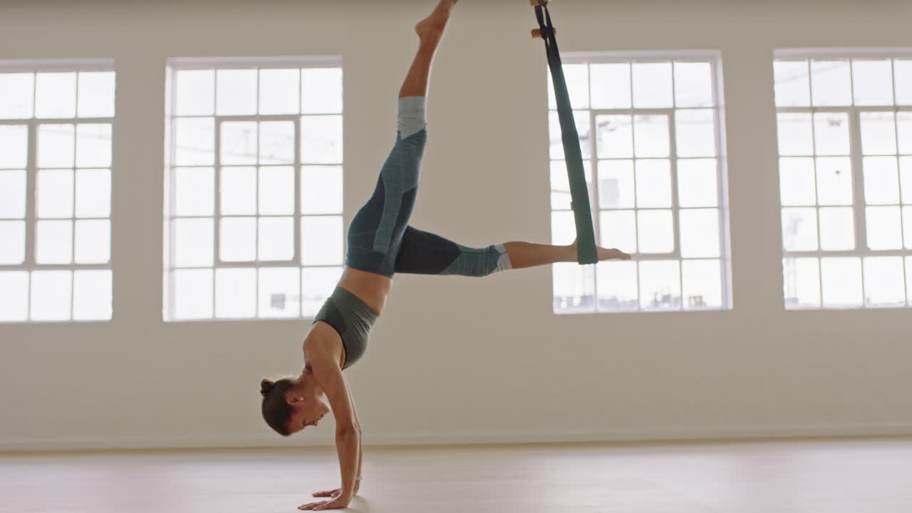 공중 요가 여자가  ⁇ 드스탠드 포즈를 연습하고 망토를 사용하고 건강한 피트니스 라이프 스타일을 즐기고 스튜디오에서 운동하고 해가 뜨면 명상하고 있습니다.