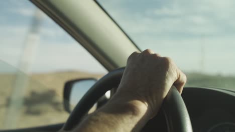 cu of man's hand on steering wheel in desert