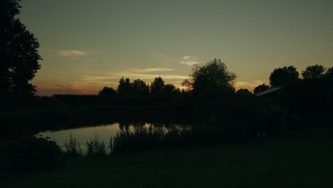 Shadows-darken-at-pond-scene-as-sun-drops-in-night-sky-timelapse