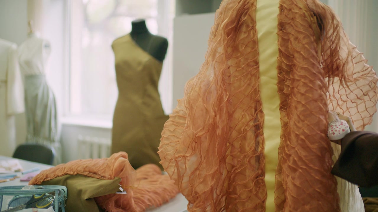 Vêtement en organza orange translucide avec des détails cousus ondulés en relief, exposé sur un mannequin de couture dans un atelier de création de mode