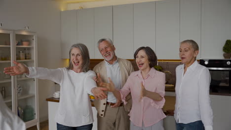 group of cheerful senior friends greeting each other with hugs in the kitchen 1