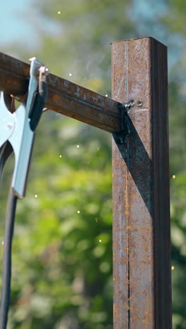 builder in protective work wear welds metal plank fixed with clamp to fence pole against blue sky on day