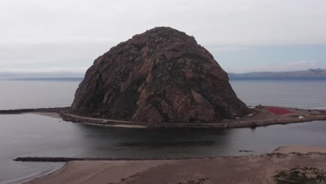 Aerial-low-panning-shot-of-Morro-Rock-at-the-end-of-the-narrow-causeway-in-Morro-Bay,-California