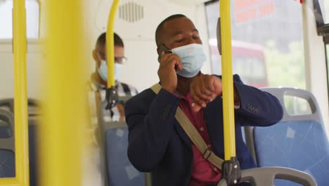 hombre afroamericano en la ciudad con cara, usando teléfono inteligente y reloj inteligente en el autobús